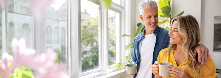 Happy older couple standing at window with mugs