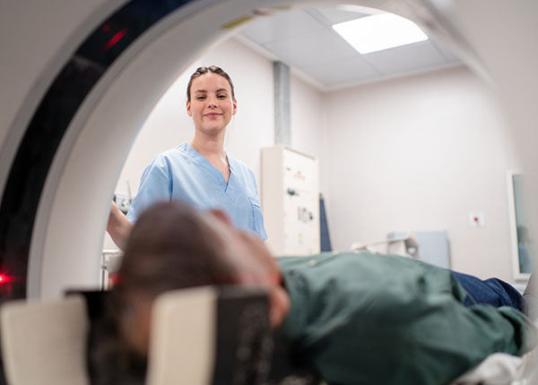 radiographer looking inside CT scan machine helping patient laying on the bed