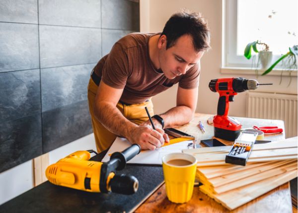 man installing wall panels with power tools writing on work bench